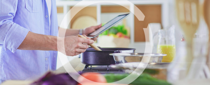 Man following recipe on digital tablet and cooking tasty and healthy food in kitchen at home.