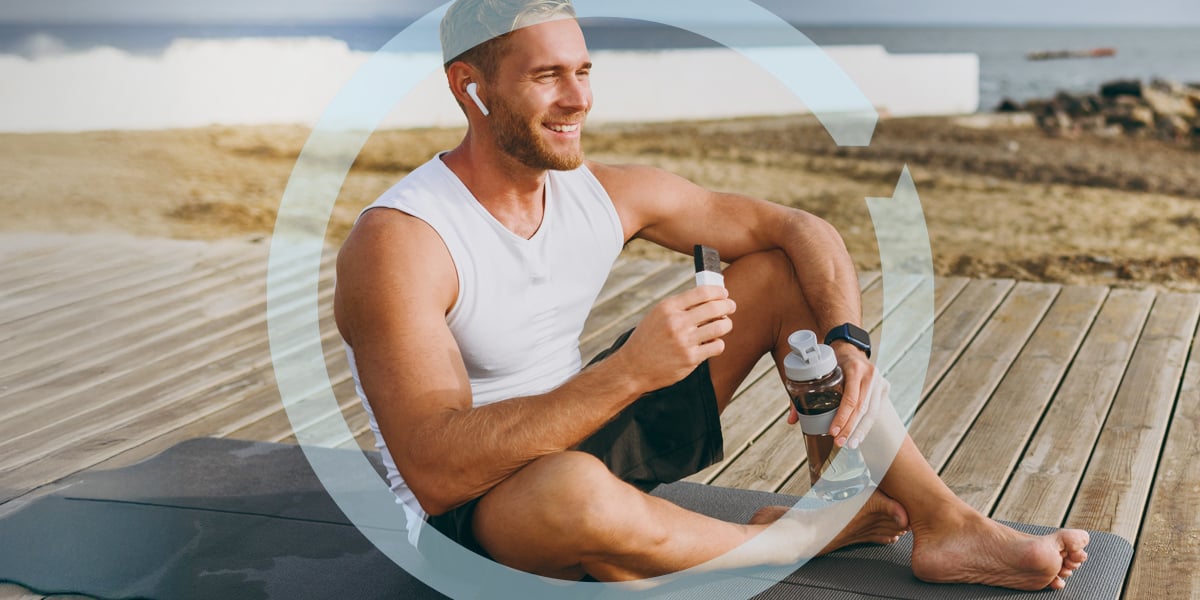 Young, athletic man on beach dock holding a protein bar and bottle of water